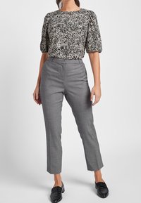 Zwart-witte bloemenblouse met poffende mouwen, gecombineerd met hoge, op maat gemaakte grijze broeken. Glad stof met een aansluitende pasvorm.