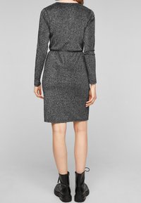 Grå stickad klänning med långa ärmar, figursydd midja och knälång fåll. Har en subtil lyster och är kombinerad med svarta snörboots.