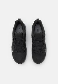 Czarne buty sportowe z teksturowanymi panelami z siateczki, elastycznymi podeszwami i wzmocnionymi oczkami. Zawierają oznaczenia marki na języku i akcenty po bokach.