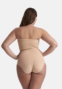 Donna con capelli lunghi e mossi vista di spalle, che indossa un top bandeau senza spalline color nudo e culotte a vita alta su uno sfondo neutro.