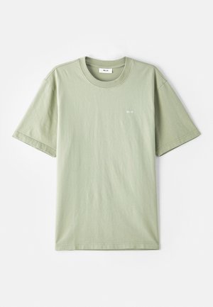 T-shirt en coton vert clair avec manches courtes, col rond et petit logo blanc sur la poitrine. Texture douce, coupe décontractée et design minimal.