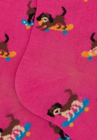 Calzini rosa con un motivo ripetuto di cani su skateboard, lavorati a maglia in colori marrone, giallo e blu con una texture liscia.