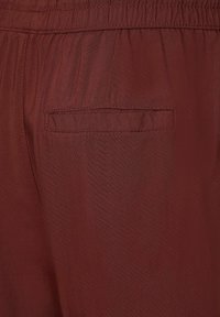 Närbild av bordo-färgade tygbyxor med elastisk midja och en bakficka med ficklock.