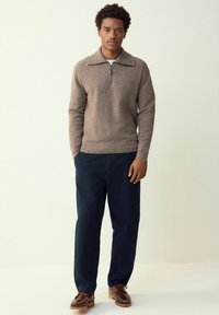 Pruun kudumiga kampsun lukuga kraega, kombineeritud tumelõuad ning pruunide kingadega. Tekstuur tundub pehme ja hubane.