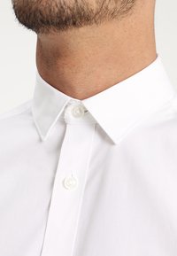 White collared shirt featuring a smooth fabric texture, button closure, and a clean, classic design. Close-up showing no patterns or accents.