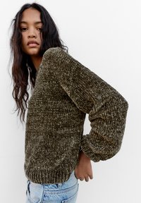 Pullover dalla texture verde oliva con orlo a coste spesso e maniche a palloncino, abbinato a jeans in denim azzurro chiaro.