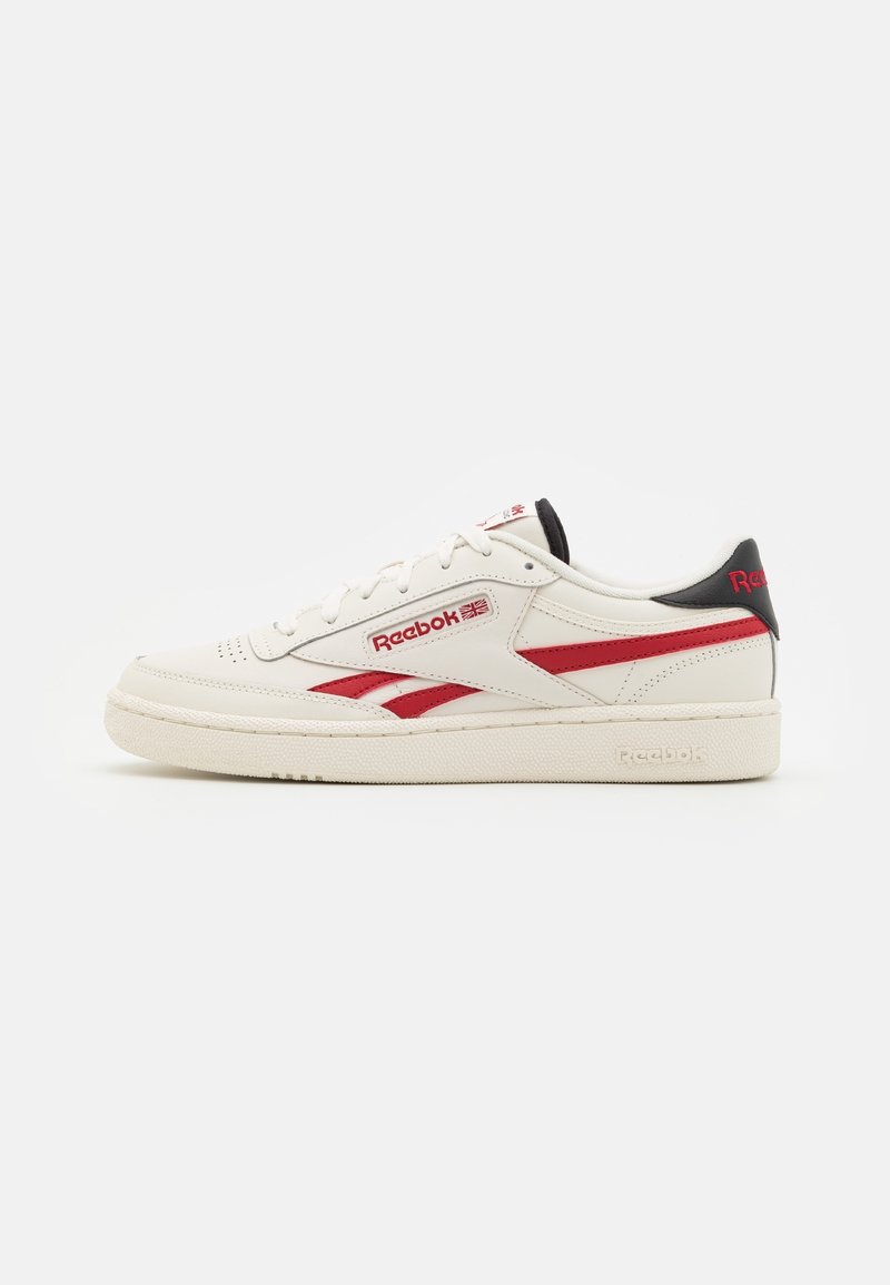 White leather sneakers with red accents, featuring a classic design, textured surface, and a rubber sole. Branding on the side and heel.