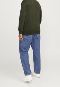 Zielony dzianinowy sweter z długimi rękawami, zestawiony z luźnymi niebieskimi jeansami i białymi trampkami, widoczny od tyłu na jasnym tle.