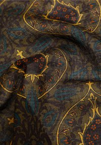 Tejido de fibras entrelazadas que presenta intrincados patrones paisley en tonos marrón oscuro, azul verdoso, dorado y rojo, con una apariencia suave y texturizada, y un rico contraste de colores.