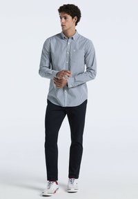 Gestreepte overhemdd met lichtblauw en wit, met een kraag en borstzak, gecombineerd met donkere broeken en witte sneakers.