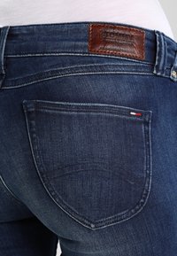 Jeans de mezclilla azul oscuro con un diseño clásico, un parche de cuero en la parte trasera con la marca y un bolsillo trasero.