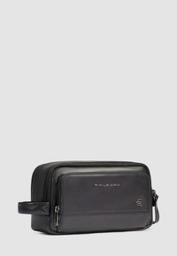 Tracolla da toeletta in pelle nera con texture liscia, chiusura a zip, tasca frontale e maniglia laterale. Presenta un dettaglio del logo impressa.