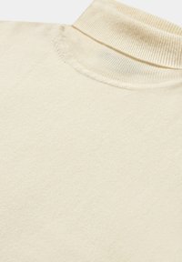 Beżowy sweter z golfem, z prążkowanym kołnierzem, wykonany z miękkiego materiału. Widoczne szwy wzdłuż dekoltu i ramion.