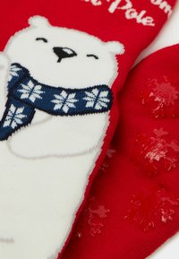 Rote Fäustlinge mit einem weißen Polarbärmotiv, der einen blauen Schal trägt. Die Handfläche ist mit erhabenen roten Schneeflockenmustern für besseren Halt versehen.