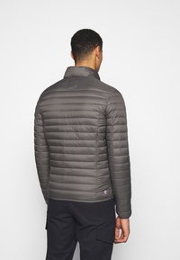 Grijze pufferjack met horizontaal doorgestikte design, staande kraag en een logo-detail aan de zoom. Gladde textuur en aangesloten silhouet.
