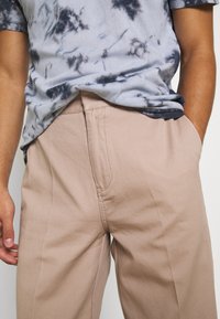 Camiseta de tie-dye azul claro combinada con pantalones beiges. Los pantalones tienen una textura suave y bolsillos laterales, con detalles de costura visibles.