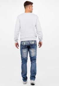 Sweatshirt gris avec des manches longues, associé à un jean en denim bleu clair comportant des patches décolorés et des coutures décoratives sur les poches arrière.