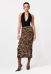 Czarny body na szyję na ramiączkach w połączeniu z spódnicą o długości do połowy łydki wykonaną z teksturowanej, brązowawej tkaniny ozdobionej kwiatowymi wzorami. Brązowe, szpiczaste szpilki.