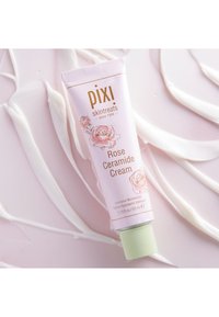 Rosa tube av Pixi Rose Ceramide Cream med grønn kork, prydet med roseillustrasjoner og gulltekst, plassert på en kremet, teksturert bakgrunn.