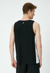 Sort atletisk tanktop med scoop-udskæring og en kontrasterende hvid sidepanel. Lavet af glat, strækbart stof. Logo nær halsudskæringen.