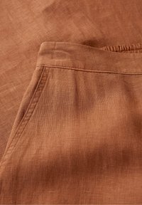 Brown linen fabric featuring a smooth texture with a subtle weave pattern, showcasing a seam and pocket detail in the design.