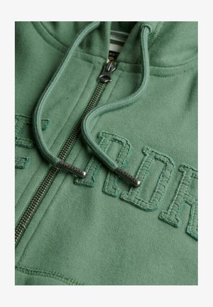 Groene rits hoodie van zacht materiaal met een voorrits en geborduurde tekst "SUPERDRY" in reliëf. Heeft een trekkoord met metallic uiteinden.