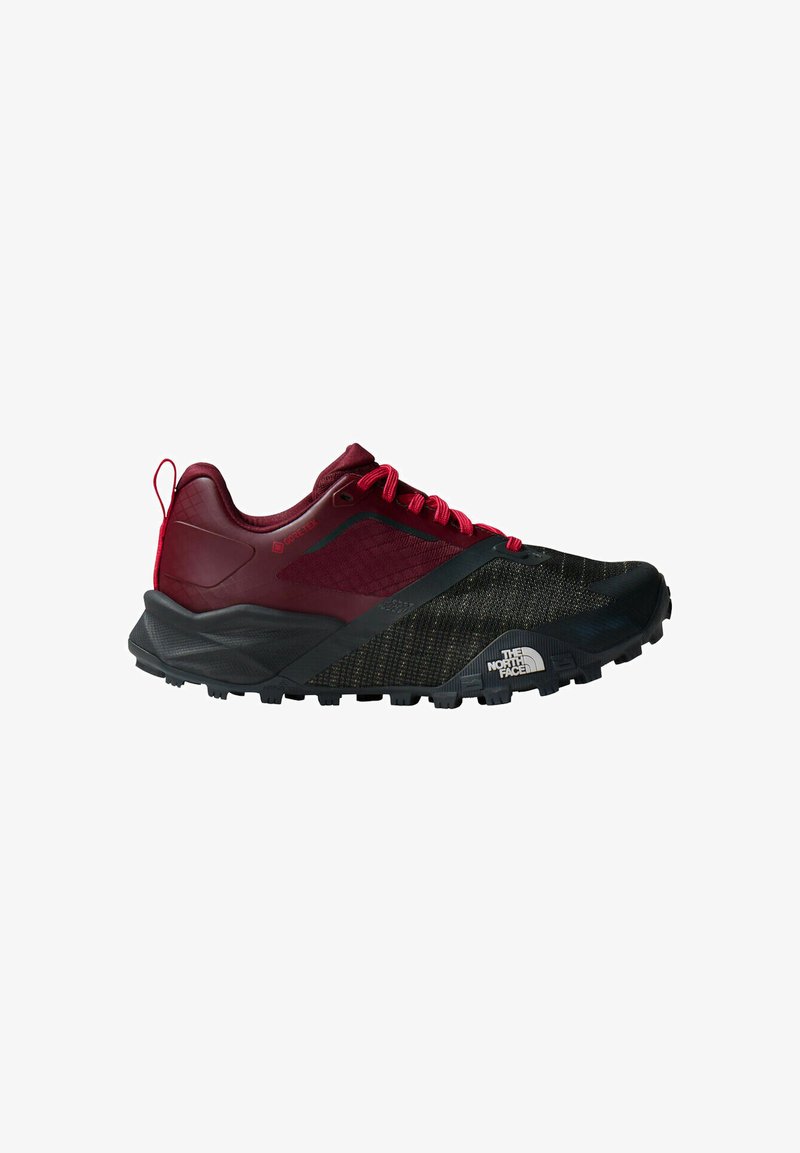 Zapatilla de trail running con parte superior negro y rojo oscuro, cordones rojos, suela rugosa, material Gore-Tex y el logo de The North Face en el lateral.