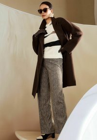 Bruine wollen jas over een wit-zwart gestreepte trui, gecombineerd met gestructureerde grijze houndstooth broek en bicolor hak schoenen.