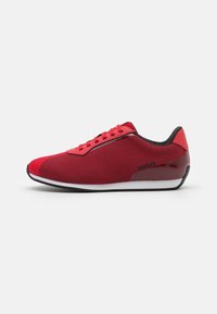 Chaussures de sport rouges avec une tige en tissu texturé, des accents noirs et une semelle blanche. Le design inclut un logo discret sur le côté.
