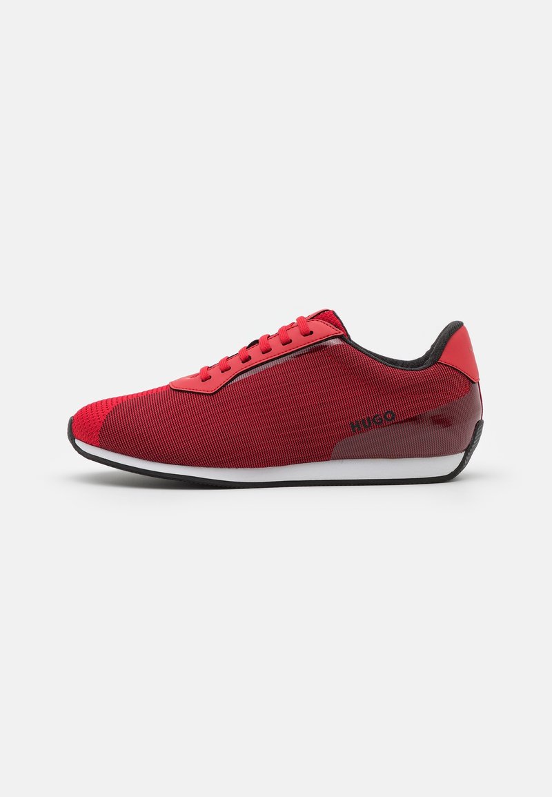 Chaussures de sport rouges avec une tige en tissu texturé, des accents noirs et une semelle blanche. Le design inclut un logo discret sur le côté.