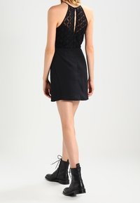 Musta mekko pitsipuvulla, halterneck-muotoilu ja levenevä hame. Yhdistetty mustien nauhattomien nilkkabootsien kanssa.