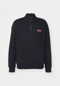Pullover nero a maniche lunghe con mezzo zip, polsini e orlo a coste, e logo rosso "HUGO" sul lato sinistro del petto.
