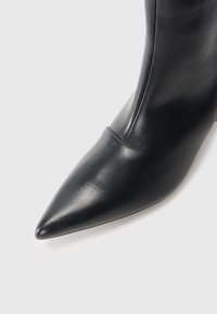 Stivale alla caviglia in pelle nera con punta affusolata, superficie liscia e dettagli di cucitura verticale lungo il lato. Tacco alto e stretto.