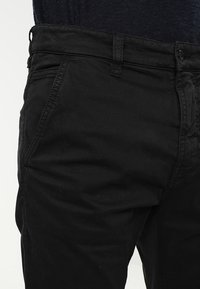 Černé bavlněné kalhoty slim fit s předními kapsami, zapínáním na knoflík a texturovaným povrchem. Jemný šev.