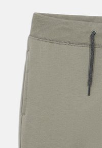 Lichtgrijze joggerbroek met geribbelde elastische tailleband, verstelbare trekkoord en gladde textuur. Voorzien van zijzakken voor extra gemak.