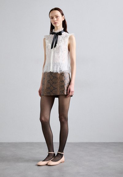 Witte kanten mouwloze top met rimpelende randen en een zwarte strik, gecombineerd met een bruin minirok met slangpatroon en doorschijnende zwarte panty's, afgewerkt met roze ballerina's.