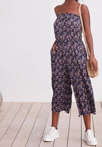 Námornícky květinový overal s elastickým vrškem, širokými nohavicemi a bočními kapsami, doplněný bílými teniskami a tkanou crossbody taškou.