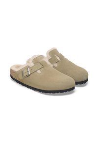 Zuecos de ante beige con detalle de hebilla, forro interior suave y suela de goma negra texturizada. Puntera redondeada y diseño sin tacón.