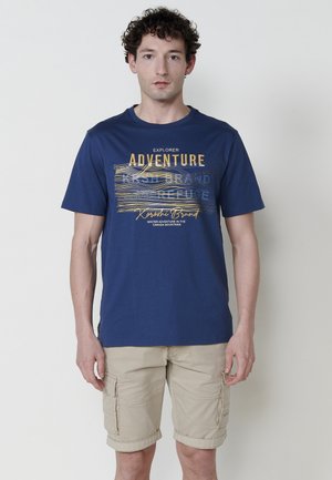 Mornarski pamučni T-shirt s grafičkim dizajnom u žutoj i plavoj boji, s natpisom "Explorer Adventure" i "Karoshti Brand."