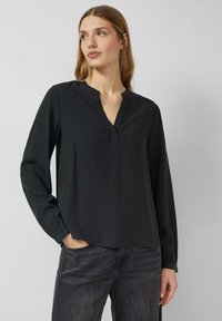 Schwarze Bluse mit langen Ärmeln und Reverskragen, aus weichem Stoff, mit lockerem Schnitt und einfachem Design. Kombiniert mit dunkelblauen Jeans.