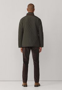 Tamnozeleni jastučići kaput s smešnim ovratnikom, u kutijastom obliku. Uparen s tamnim hlačama i smešnim obućom. Pogled sa leđa.