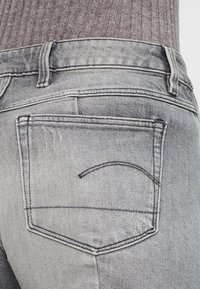 Jeans de mezclilla gris con una textura ligeramente desgastada, que cuentan con un bolsillo trasero con un detalle de costura curvada y costuras reforzadas en los bordes.
