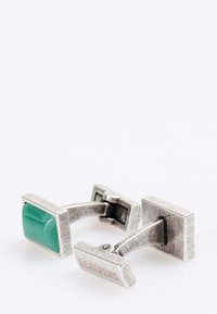 Gemelos de plata con una piedra verde, diseño rectangular, acabado texturizado y grabado de marca en un lado.