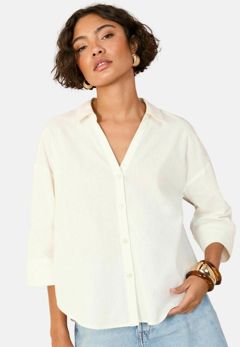 Camicia colore crema, con bottoni, realizzata in tessuto leggero, con scollo a V, maniche lunghe e una vestibilità rilassata con orlo curvo.