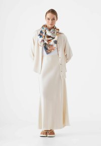 Crème kleurige satijnen maxi rok gecombineerd met een bijpassende blouse met knopen en een bloemenzijde sjaal met blauwe, oranje en groene accenten.