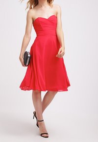 Uden skulderremme rød cocktailkjole i letvægtsstof, med en tætsiddende liv og udprægt nederdel. Glat tekstur med vandrette plisseringer.