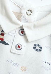 Camisa polo blanca con un diseño con cuello, dos botones con acentos rojos y patrones de temática náutica, incluyendo faros y boyas de salvamento.