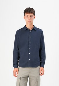 Marineblauwe overhemeld shirt met een gestructureerde stof, lange mouwen en een kraag. Beschikt over witte knopen en een relaxed fit.