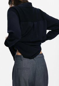 Marineblauw shirt met een gestructureerd schouderstuk, gecombineerd met grijze, op maat gemaakte broek met achterzakken en een gladde afwerking.
