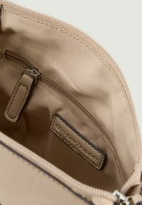 Bustina beige con zip, dotata di un esterno in pelle liscia, una fodera in tessuto beige e una piccola tasca interna con zip metallica e una toppa con logo.